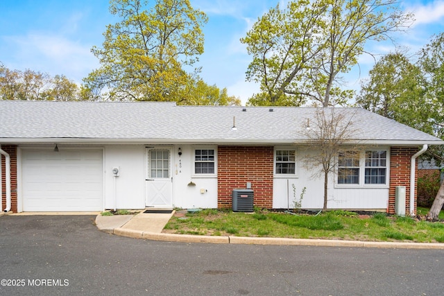 exterior space with roof with shingles, a garage, brick siding, cooling unit, and aphalt driveway