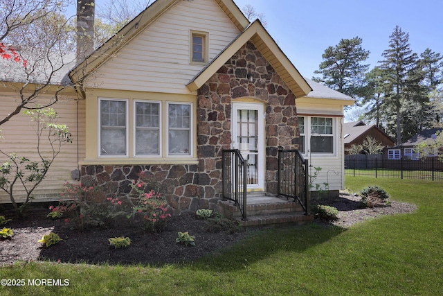 bungalow-style home with fence, a front yard, and stone siding