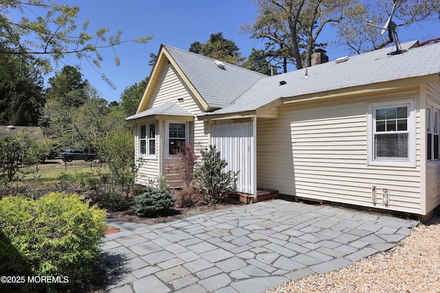 rear view of property with a shingled roof, a patio area, fence, and a chimney