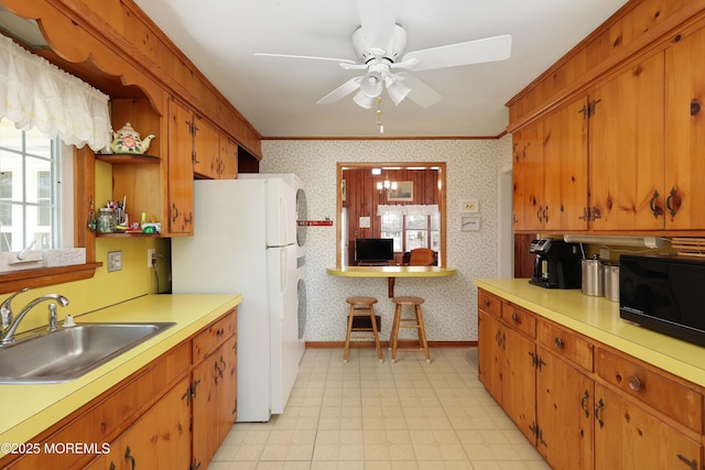 kitchen with black microwave, a sink, freestanding refrigerator, wallpapered walls, and light floors