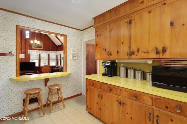 kitchen with crown molding, an inviting chandelier, light countertops, wallpapered walls, and baseboards