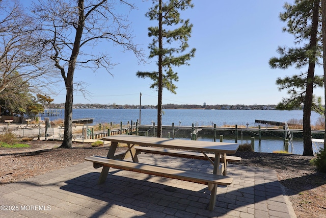 surrounding community featuring fence, a boat dock, a water view, and a patio