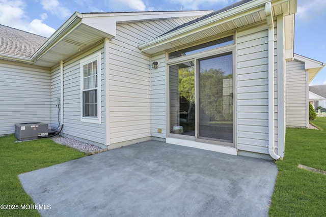 property entrance featuring a lawn, a patio area, roof with shingles, and cooling unit