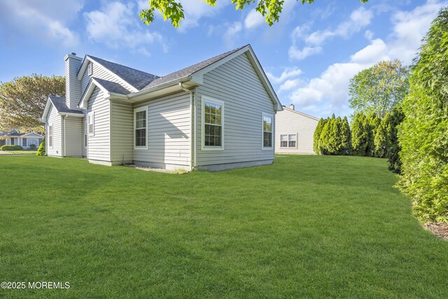back of house featuring a lawn, a shingled roof, and a chimney