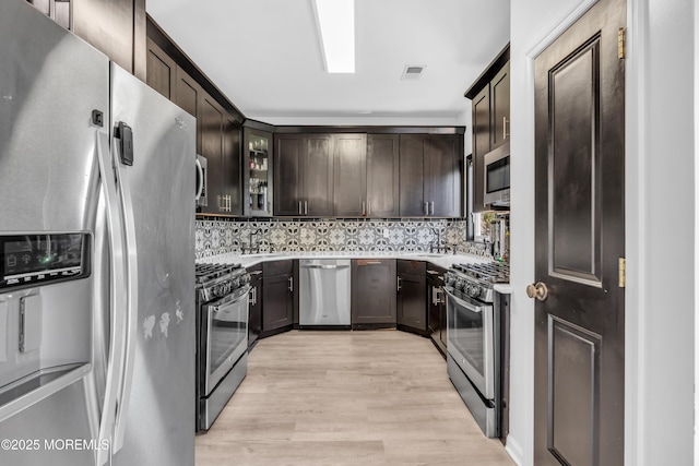kitchen with dark brown cabinets, light countertops, light wood-style flooring, stainless steel appliances, and visible vents