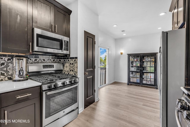kitchen featuring dark brown cabinetry, appliances with stainless steel finishes, light wood-style floors, light countertops, and backsplash