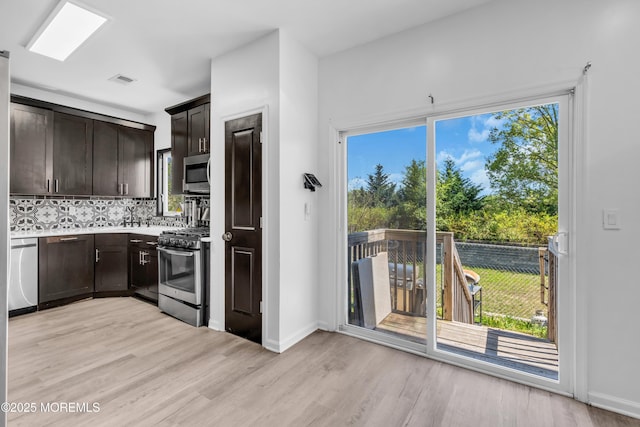 kitchen with backsplash, dark brown cabinets, appliances with stainless steel finishes, and light wood finished floors