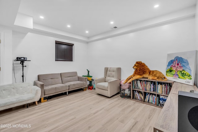 living area with a raised ceiling, recessed lighting, wood finished floors, and visible vents