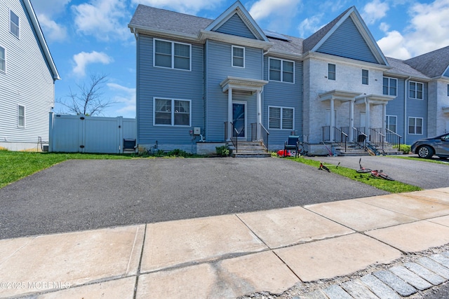 multi unit property with fence, a gate, roof with shingles, and aphalt driveway