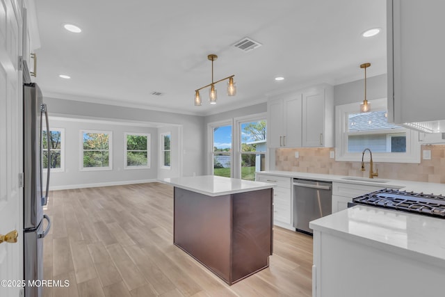 kitchen with a sink, white cabinets, ornamental molding, and stainless steel appliances