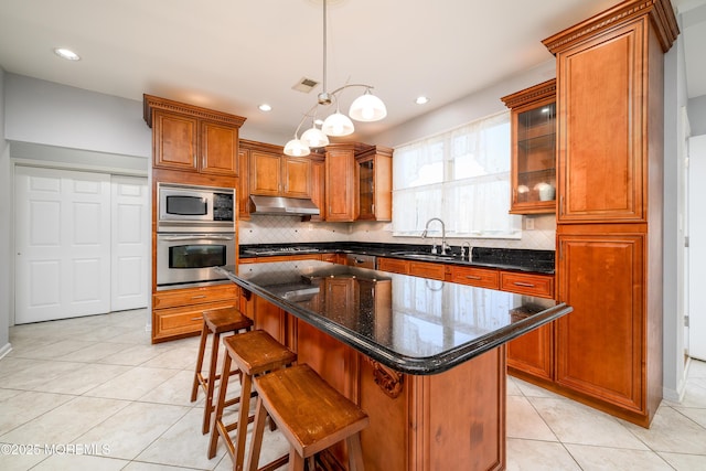 kitchen featuring brown cabinetry, a sink, under cabinet range hood, and stainless steel appliances