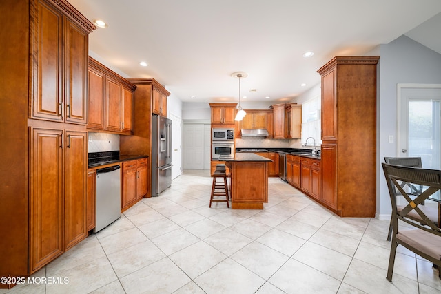 kitchen featuring dark countertops, appliances with stainless steel finishes, brown cabinets, a sink, and a breakfast bar