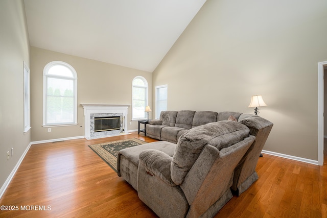 living room featuring light wood-style floors, high vaulted ceiling, baseboards, and a premium fireplace