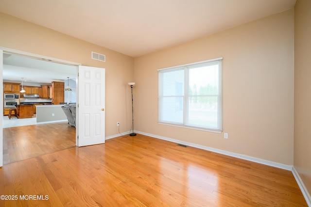 empty room with visible vents, light wood finished floors, and baseboards
