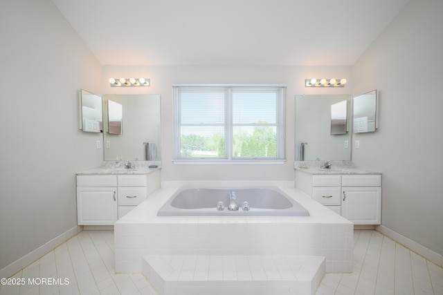 bathroom with baseboards, a bath, tile patterned floors, two vanities, and a sink