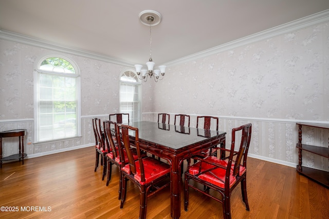 dining area with an inviting chandelier, ornamental molding, wallpapered walls, and wood finished floors