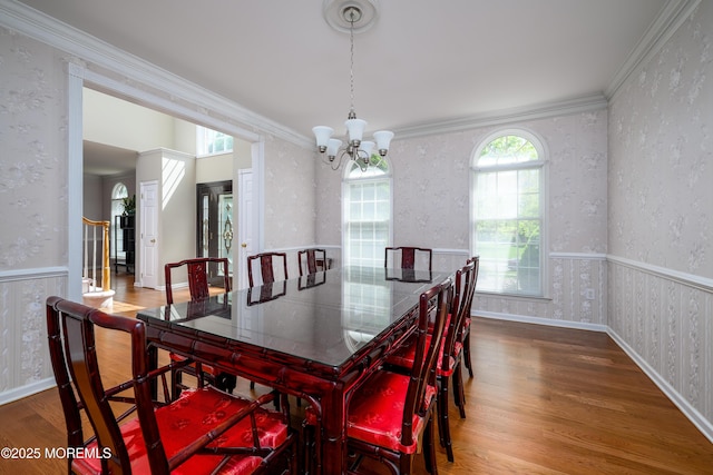 dining space with an inviting chandelier, wainscoting, wood finished floors, and wallpapered walls