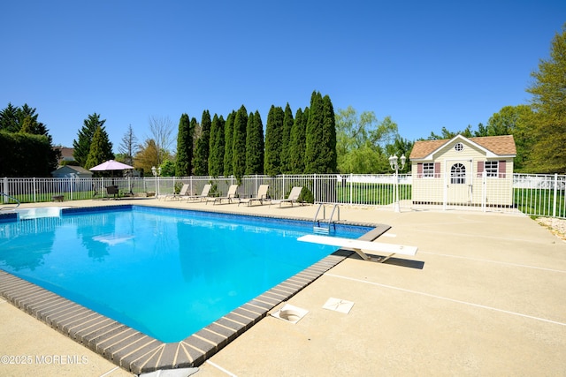 view of pool featuring fence, a diving board, a fenced in pool, an outbuilding, and a patio area