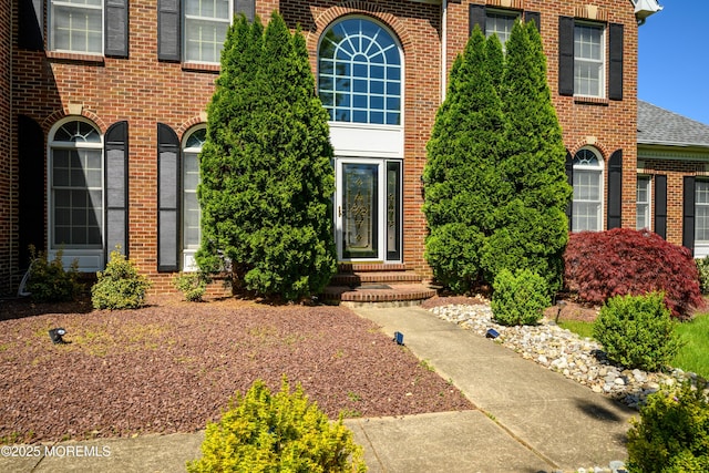 entrance to property featuring brick siding and roof with shingles
