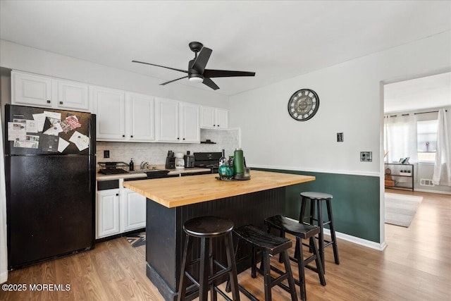 kitchen with butcher block countertops, freestanding refrigerator, a breakfast bar area, and white cabinets