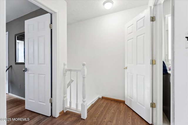 corridor featuring baseboards, a textured ceiling, wood finished floors, and an upstairs landing