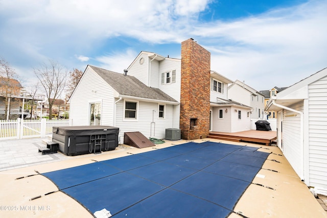 back of property featuring a chimney, a wooden deck, a hot tub, fence, and a patio