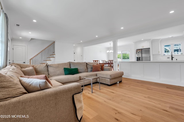 living area with light wood-type flooring, stairs, recessed lighting, a chandelier, and ornate columns