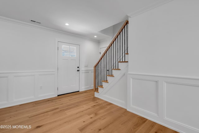 entryway featuring a decorative wall, ornamental molding, stairway, light wood-style floors, and a wainscoted wall