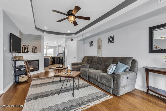 living area with ceiling fan, wood finished floors, baseboards, a glass covered fireplace, and recessed lighting