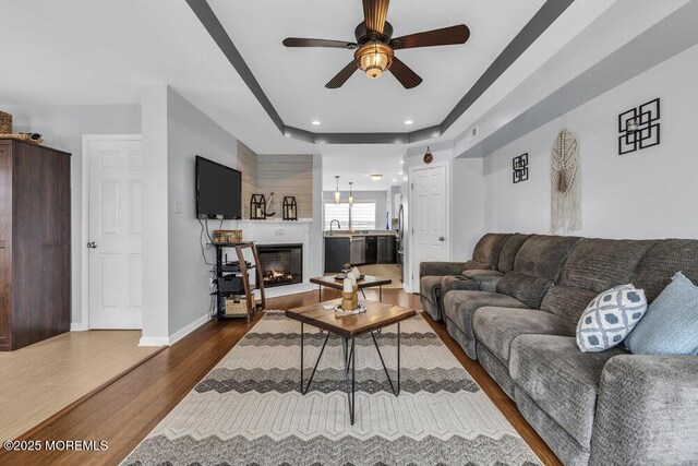 living room with dark wood finished floors, a glass covered fireplace, a ceiling fan, baseboards, and recessed lighting