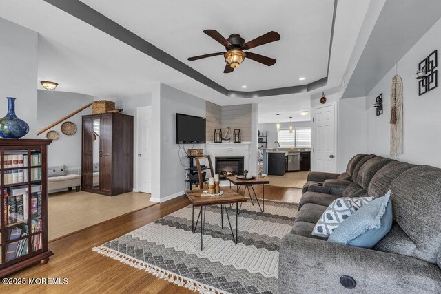 living room with a ceiling fan, a warm lit fireplace, wood finished floors, and a raised ceiling