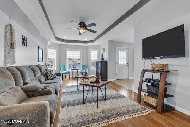 living room with a ceiling fan, wood finished floors, baseboards, a tray ceiling, and recessed lighting