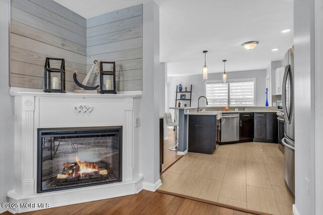kitchen featuring a sink, light countertops, a peninsula, decorative light fixtures, and stainless steel dishwasher