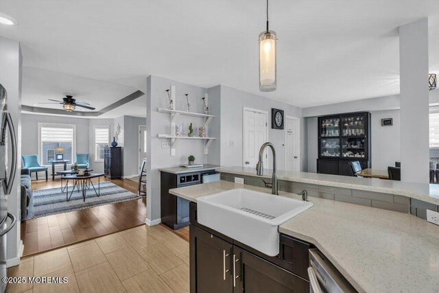 kitchen with pendant lighting, a ceiling fan, dark brown cabinets, light stone counters, and a sink