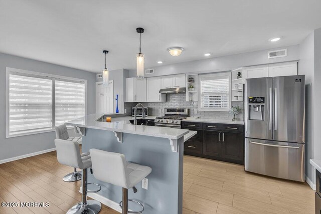 kitchen featuring a breakfast bar area, visible vents, appliances with stainless steel finishes, light countertops, and under cabinet range hood