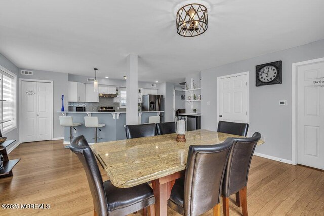 dining room with baseboards, a notable chandelier, light wood finished floors, and visible vents