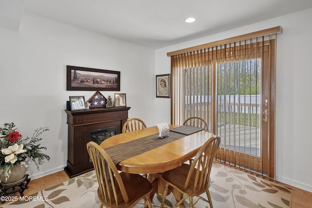 dining space with baseboards, light wood finished floors, a glass covered fireplace, and recessed lighting