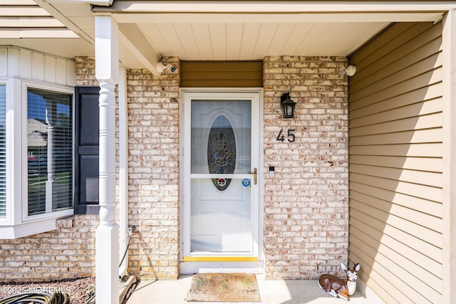 property entrance with board and batten siding, brick siding, and covered porch