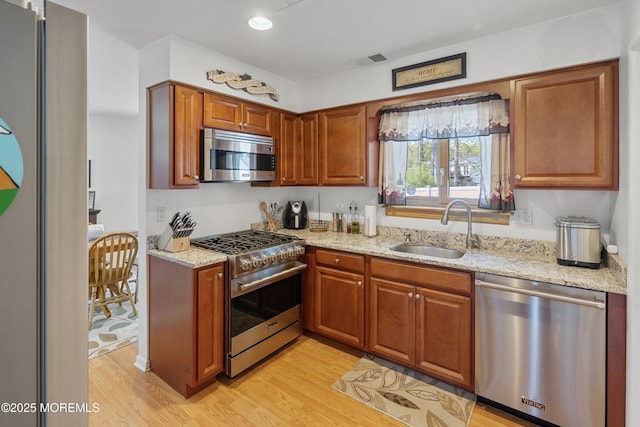 kitchen with light wood-type flooring, light stone countertops, appliances with stainless steel finishes, and a sink