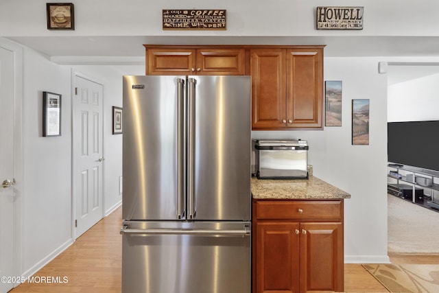 kitchen with high quality fridge, light wood-style floors, brown cabinets, and light stone countertops