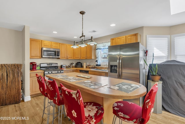 14 Dolan Ave, Aberdeen, NJ 07747 - kitchen with a breakfast bar area, a kitchen island, appliances with stainless steel finishes, a sink, and light wood-style floors