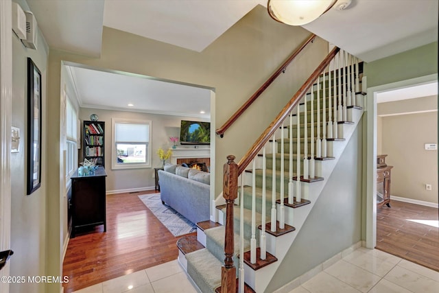 stairway featuring baseboards, ornamental molding, tile patterned floors, and a warm lit fireplace