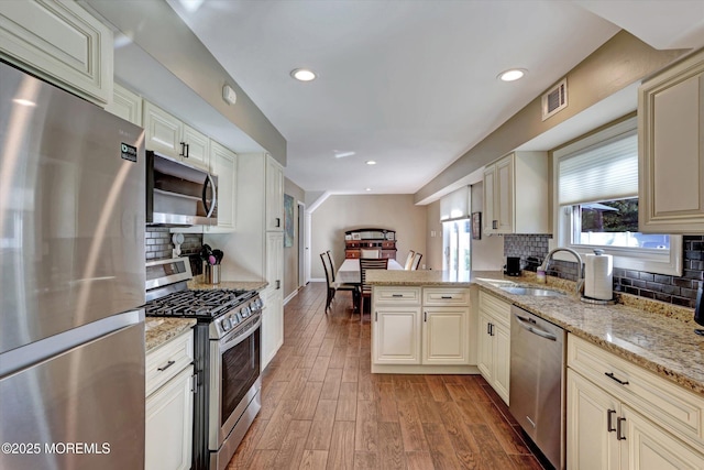 kitchen featuring appliances with stainless steel finishes, a sink, light wood-style flooring, a peninsula, and decorative backsplash