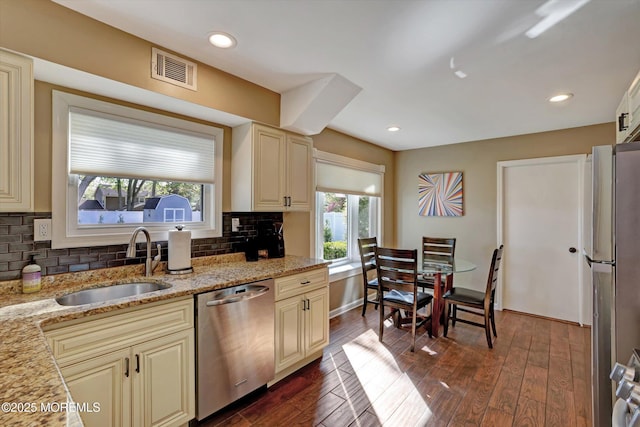 kitchen with cream cabinets, light stone counters, a sink, stainless steel appliances, and visible vents