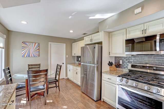 kitchen with visible vents, tasteful backsplash, light wood-type flooring, light stone counters, and stainless steel appliances