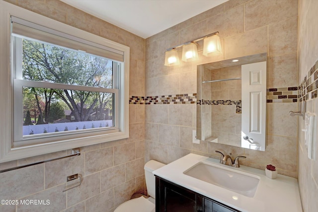 bathroom with tile walls, plenty of natural light, vanity, and toilet