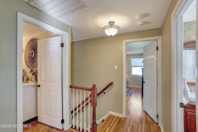 hall with baseboards, an upstairs landing, light wood finished floors, and visible vents
