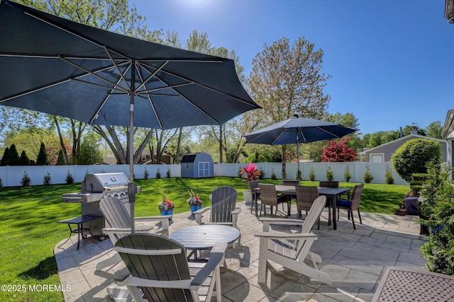 view of patio with a fenced backyard, an outbuilding, outdoor dining area, and a shed