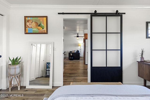 bedroom featuring a barn door, baseboards, ornamental molding, and wood finished floors