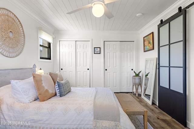 bedroom with ornamental molding, multiple closets, wood finished floors, a barn door, and wooden ceiling